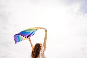 Woman with rainbow flag on sky background.