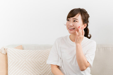 Fototapeta premium ソファに座りながら肌を触る女性（スキンケア） 