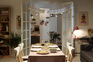 Homemade food, glasses with wine and plates on dinner table served for guests in the center of living room before celebration of birthday