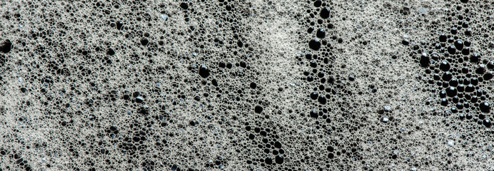Texture of white foam on a black background. Cleansing mousse for the face or shaving foam or washing powder. Closeup
