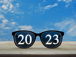 2023 white text with black eye glasses on wooden table over blue sky with white clouds, Business vision happy new year 2023 concept