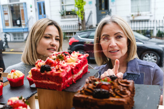 Senior woman choosing pastry with daughter seen through store window