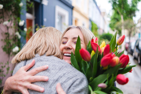 Happy senior woman with flowers embracing daughter
