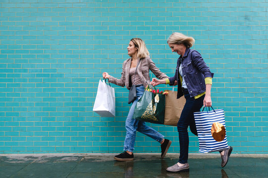 Mother and daughter with shopping bags running on wet sidewalk