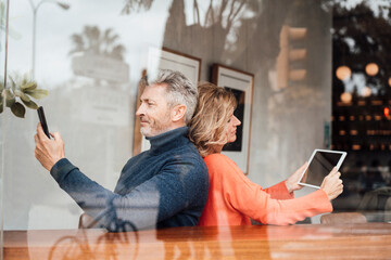 Smiling couple using wireless technologies sitting cafe seen through glass