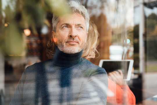 Thoughtful man sitting in front of woman using tablet PC in cafe