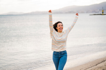 Happy woman with arms raised walking on beach
