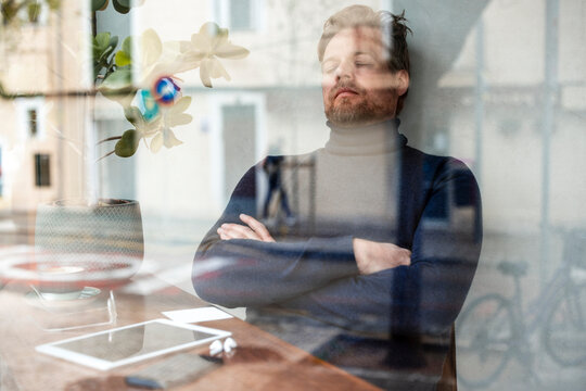 Businessman with arms crossed relaxing in cafe seen through glass window