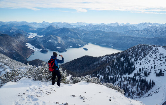 Hiker photographing Walchensee and Bavarian Prealps from Mt. Herzogstand, Bavaria, Germany