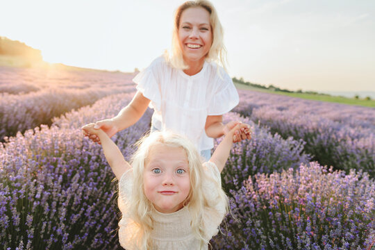 Happy mother playing with daughter in lavender field at sunset
