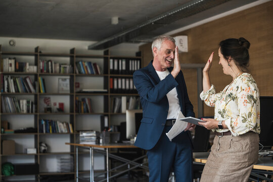 Happy business colleagues giving high-five standing by desk in office