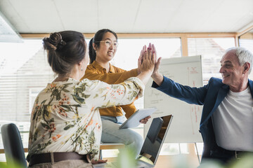 Successful business colleagues giving high-five to each other in office