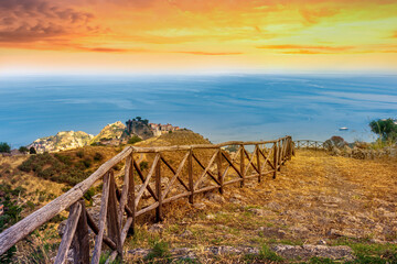 mountain landscape with a hiking trail leading to a mountain town and beautiful blue seashore far away