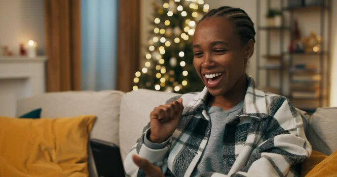 Winter evening. An African-looking girl has video chat with parents. She greeted, was glad to hear them, talked and smiled. At the end of the conversation, girl said goodbye and waved.