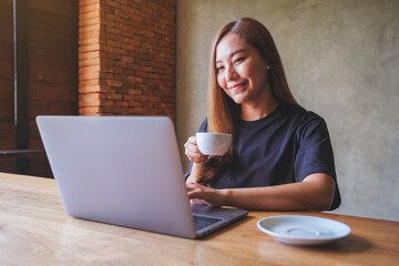 Fototapeta premium Portrait image of a young woman working on laptop computer while drinking coffee