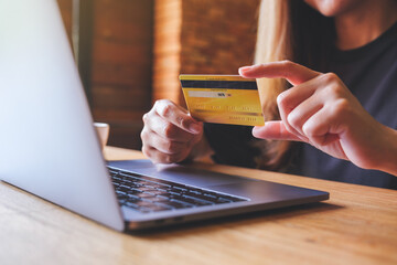 Closeup image of a woman holding credit cards while using laptop computer for online payment