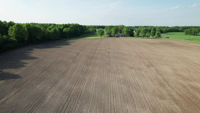 Slow motion drone view of beautiful farm land with sprawling spacious green fields, lots of trees and shrubs under a blue sky. Farming natural surroundings.