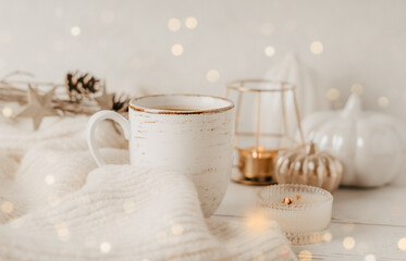 Details of Still life, cup of tea or coffee, pumpkins, candle, brunch with leaves on white table background, home decor in a cozy house. Autumn weekend concept. Fallen leaves and home decoration