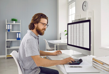 Entrepreneur or business accountant working on office computer. Side view of bearded man in T shirt...