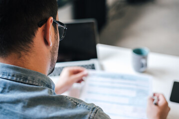 Rear view of freelancer analyzing documents while working at table