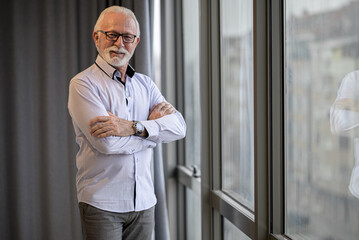 Portrait of confident senior entrepreneur standing by window at corporate office