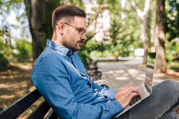 Fototapeta premium Serious entrepreneur working on laptop while sitting at park bench