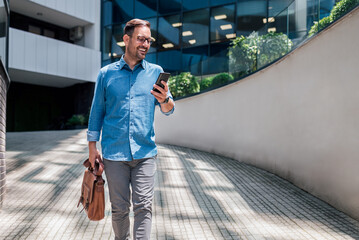 Happy professional messaging on cellphone while walking against office building