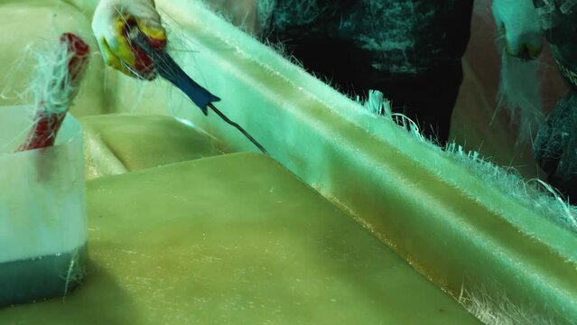 Close-up of a man working on the fiberglass treatment of the boat's hull. Construction of fiberglass pedal catamarans in a private shop