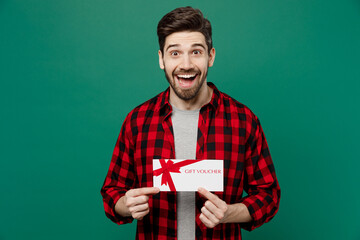 Young happy smiling caucasian man he 20s in red shirt grey t-shirt hold gift certificate coupon voucher card for store isolated on plain dark green background studio portrait People lifestyle concept