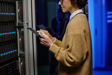 Young female engineer checking data on digital tablet while working with supercomputer in data center