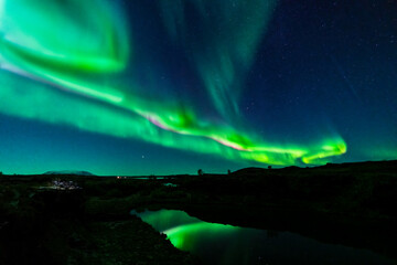 Northern lights with dark water canal and green reflections