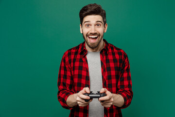 Young happy smiling caucasian man he 20s wear red shirt grey t-shirt hold in hand play pc game with...