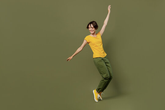 Full body young smiling happy woman she 20s wear yellow t-shirt stand on toes leaning back with outstretched hand dance isolated on plain olive green khaki background studio. People lifestyle concept.