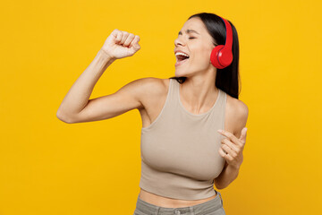 Young singer fun happy latin woman 30s she wear basic beige tank shirt headphones listen to music...