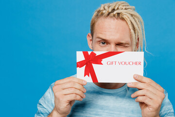 Young fun surprised blond man with dreadlocks 20s he wear white t-shirt hold cover mouth with gift...