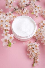 Fototapeta na wymiar Container with bodycare and skincare cream on a pink background with blooming cherry. Cosmetic facial skin care and spa. Natural treatment concept.