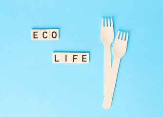 ECO LIFE sign made by wooden cubes with wooden cutlery on the side on the blue backhround. Zero waste, ecological concept.