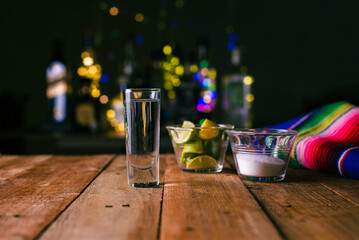 Shot of tequila served in a tequila glass on a wooden table. Blurred background. Rustic bar atmosphere. - obrazy, fototapety, plakaty