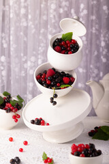Seasonal summer berry in a white bowl. Red and black currant. On the table are plates of berries floating in the air.