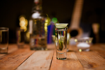 Shot of tequila served in a tequila glass on a wooden table. Blurred background. Rustic bar atmosphere.