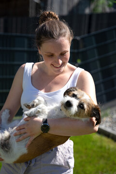 Eine junge Frau hält einen kleinen Terrier Hund auf dem Arm im Garten. Freundschaft.
