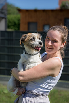 Eine junge lächelnde Frau hält einen kleinen Terrier Hund auf dem Arm im Garten. Sommer, Freundschaft.