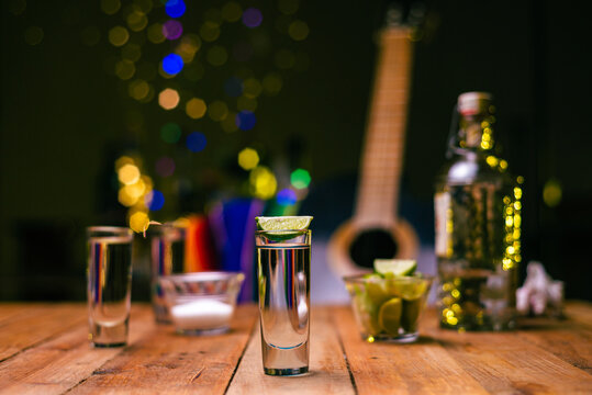 Shot of tequila served in a tequila glass on a wooden table. Blurred background. Rustic bar atmosphere.