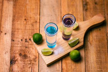 Tequila shots served in tequila glasses on a wooden table. Tequila shots with salt and lime on a bar table.