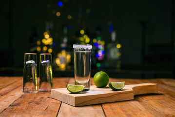 Tequila shots served in tequila glasses on a wooden table. Tequila shots with salt and lime on a...