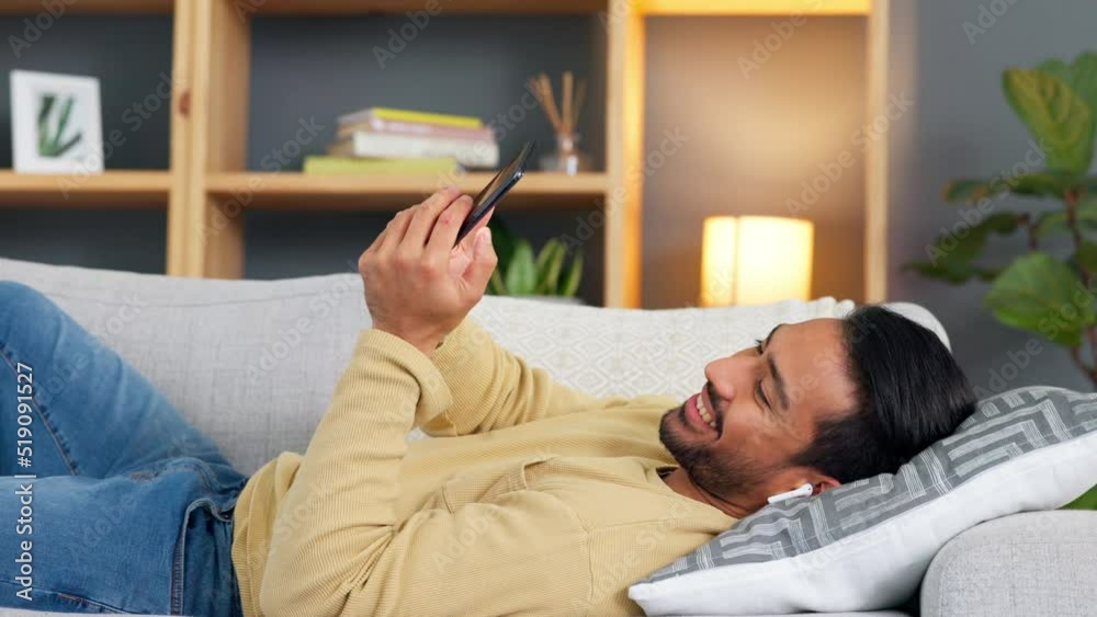 Poster relaxed man texting on his phone and listening to music in his earbuds while lying on the sofa. happ