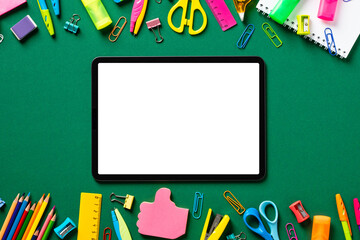 Digital tablet mockup with blank screen with school supplies on green table. Back to school, distance learning concept. Top view. Flat lay.