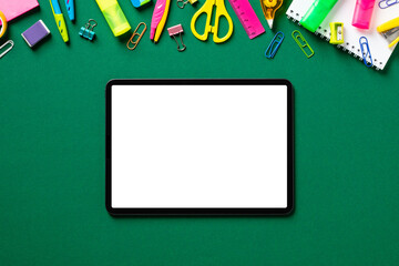 Digital tablet pad mockup with blank screen and school stationery on green table. Back to school concept. Flat lay, top view, copy space.