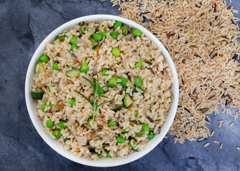 Wild and brown rice pilaf with green peas, onion and baby marrow on dark slate with raw rice and copy space

