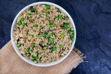 Wild and brown rice pilaf with green peas, onion and baby marrow on black slate with burlap and copy space